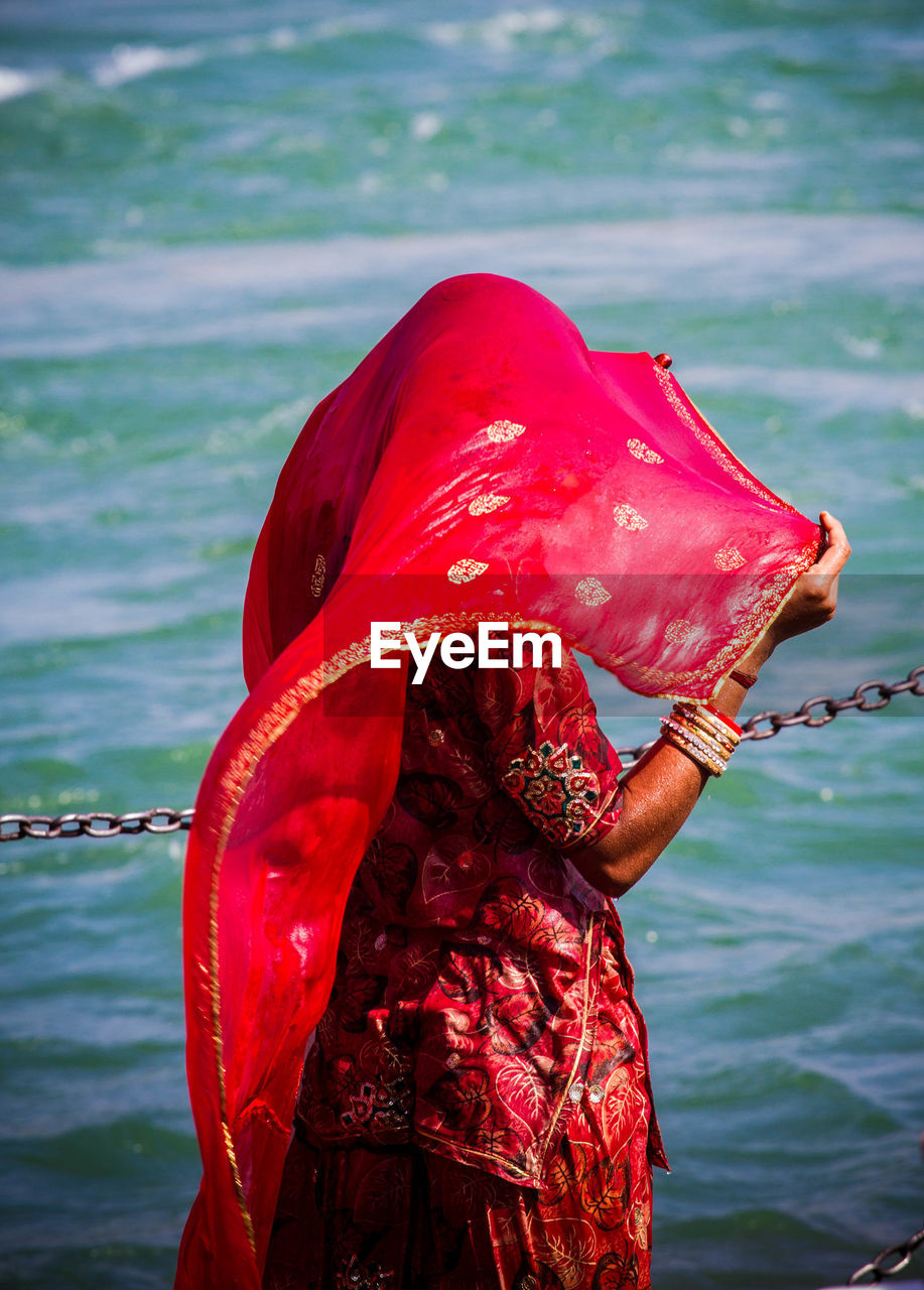 Woman in red traditional clothing standing against sea