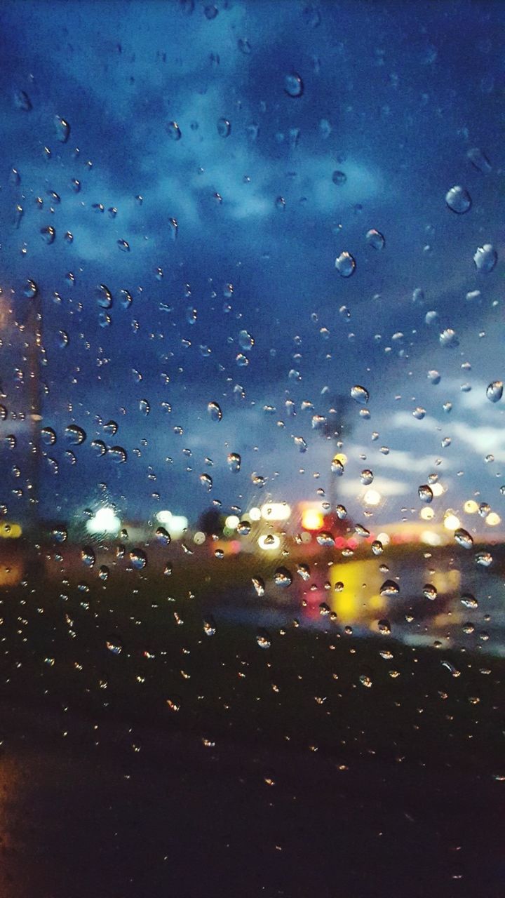 CLOSE-UP OF WET GLASS WINDOW AGAINST ILLUMINATED SKY