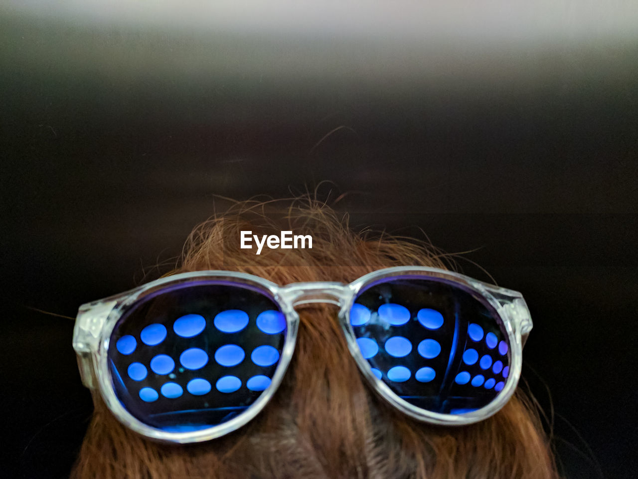 Close-up of person wearing sunglasses with reflection of blue illuminated lights