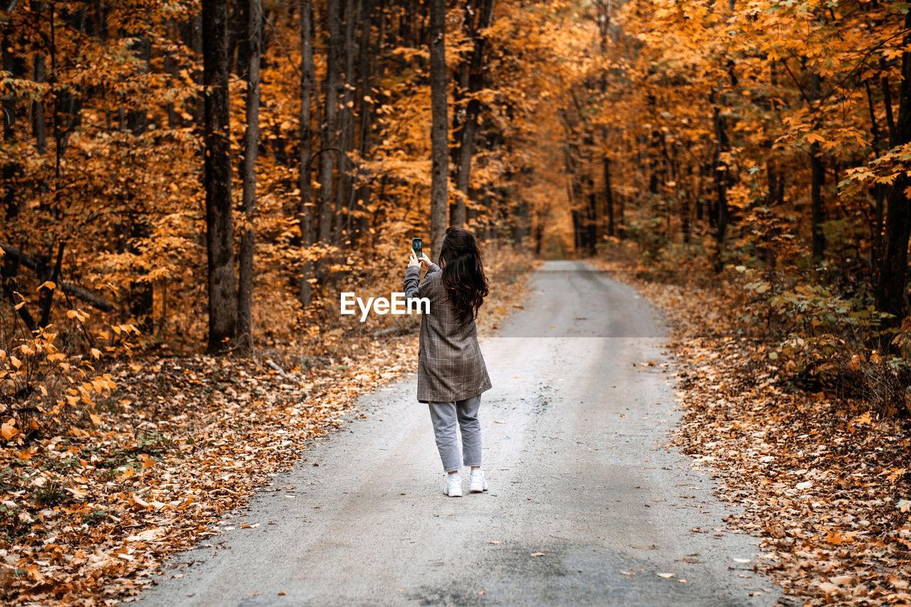 Woman taking pictures in autumn forest. mobile photography, film photography, taking photos