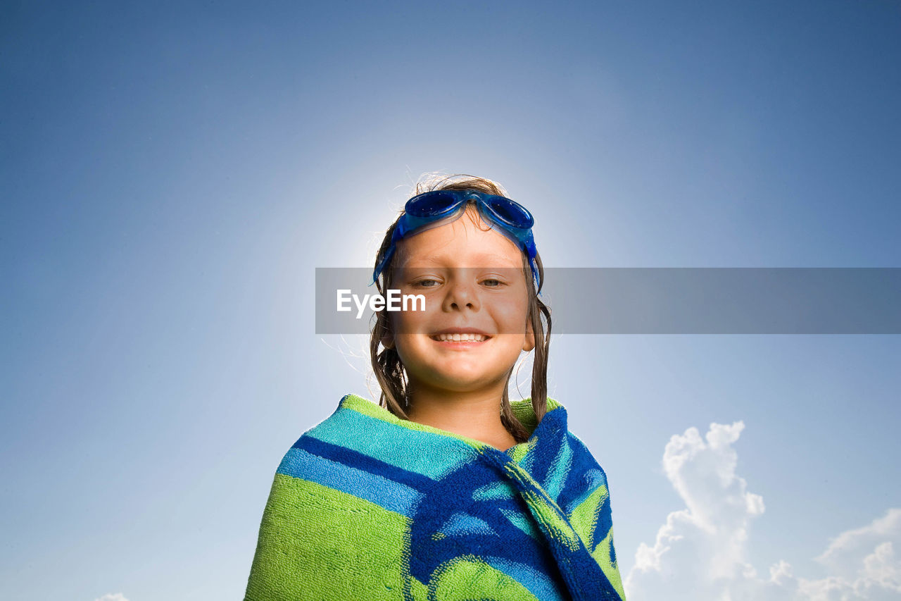 Portrait of happy girl covered with towel against sky