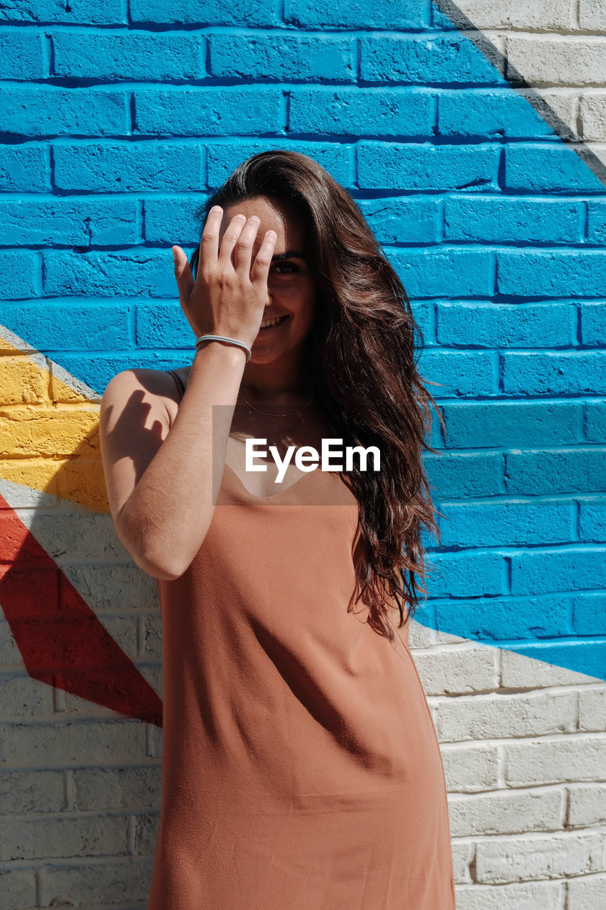 Portrait of happy young woman standing against wall