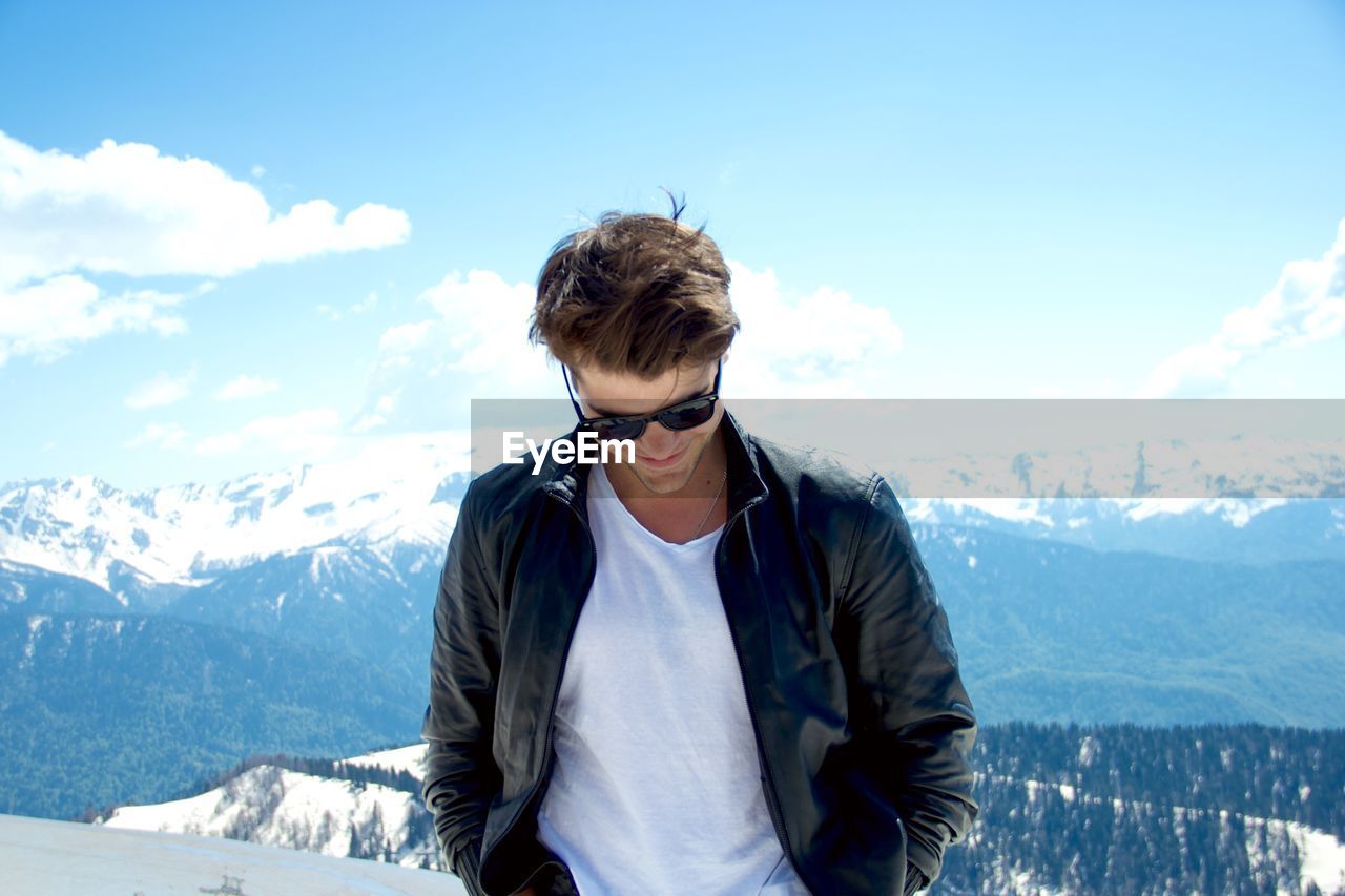 Young man wearing sunglasses while standing against snowcapped mountains