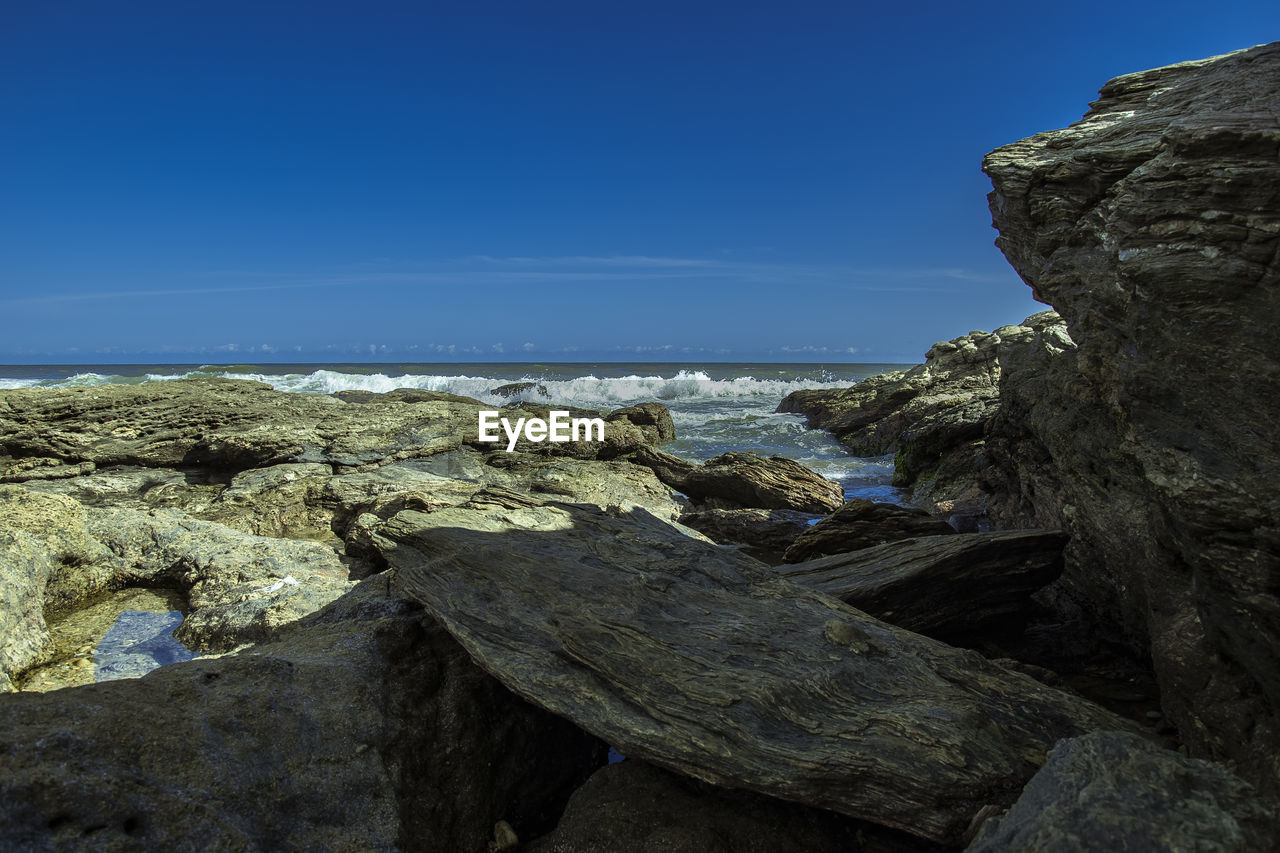 Rock formations on shore against blue sky