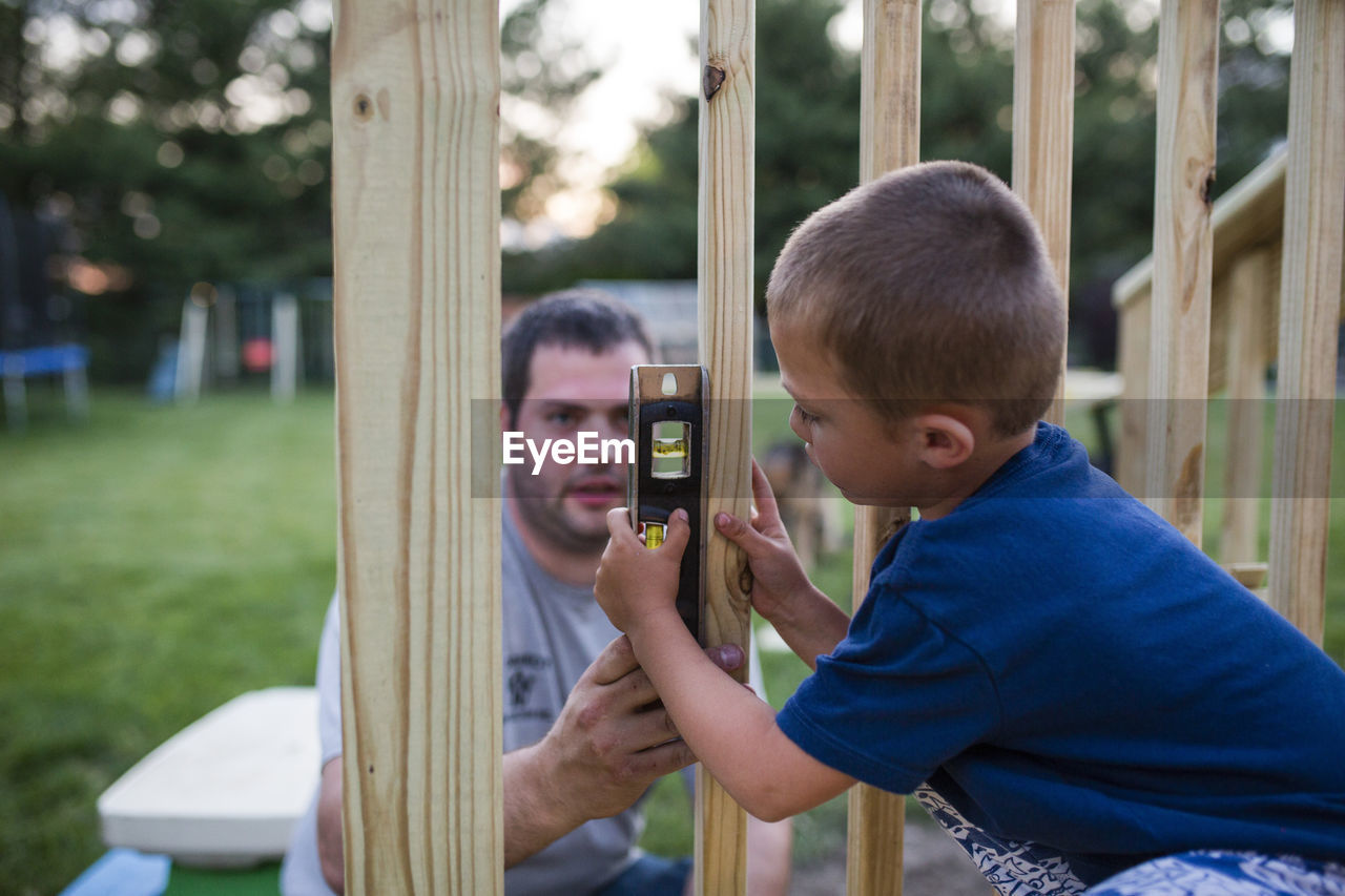 Father teaching son to use spirit level on wooden frame at yard