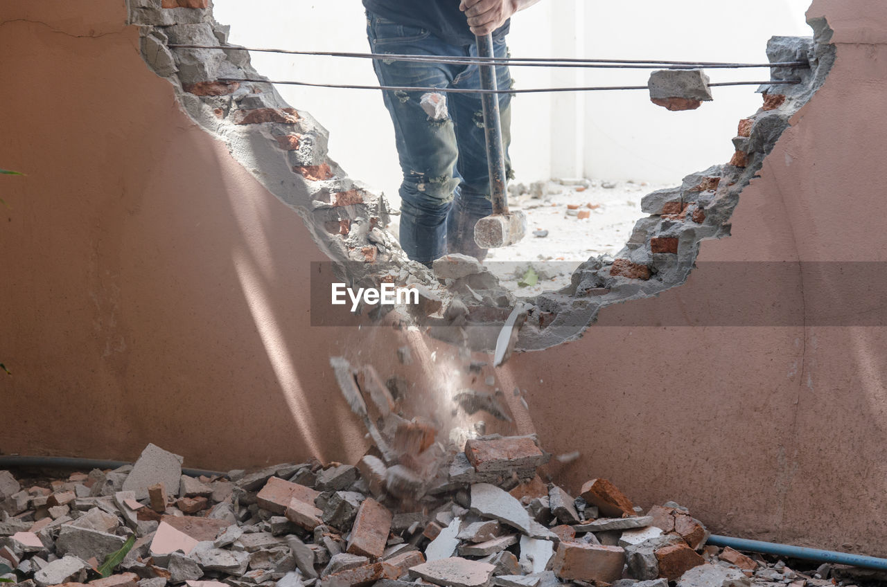 Midsection of construction worker demolishing wall with sledgehammer