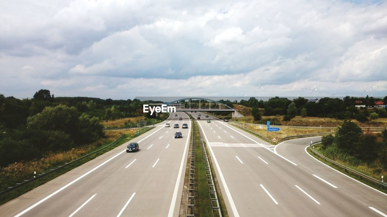 Cars on road against cloudy sky during sunny day