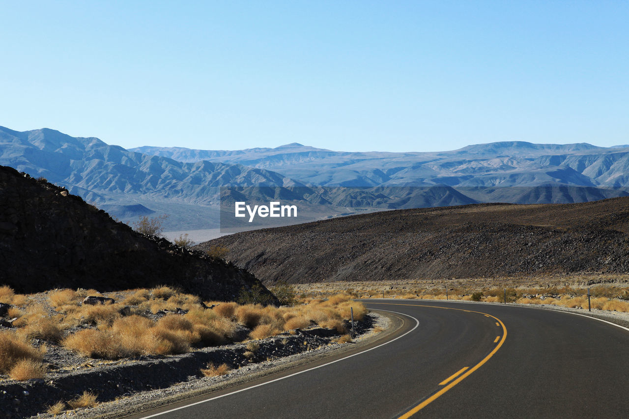 Road passing through desert against clear blue sky