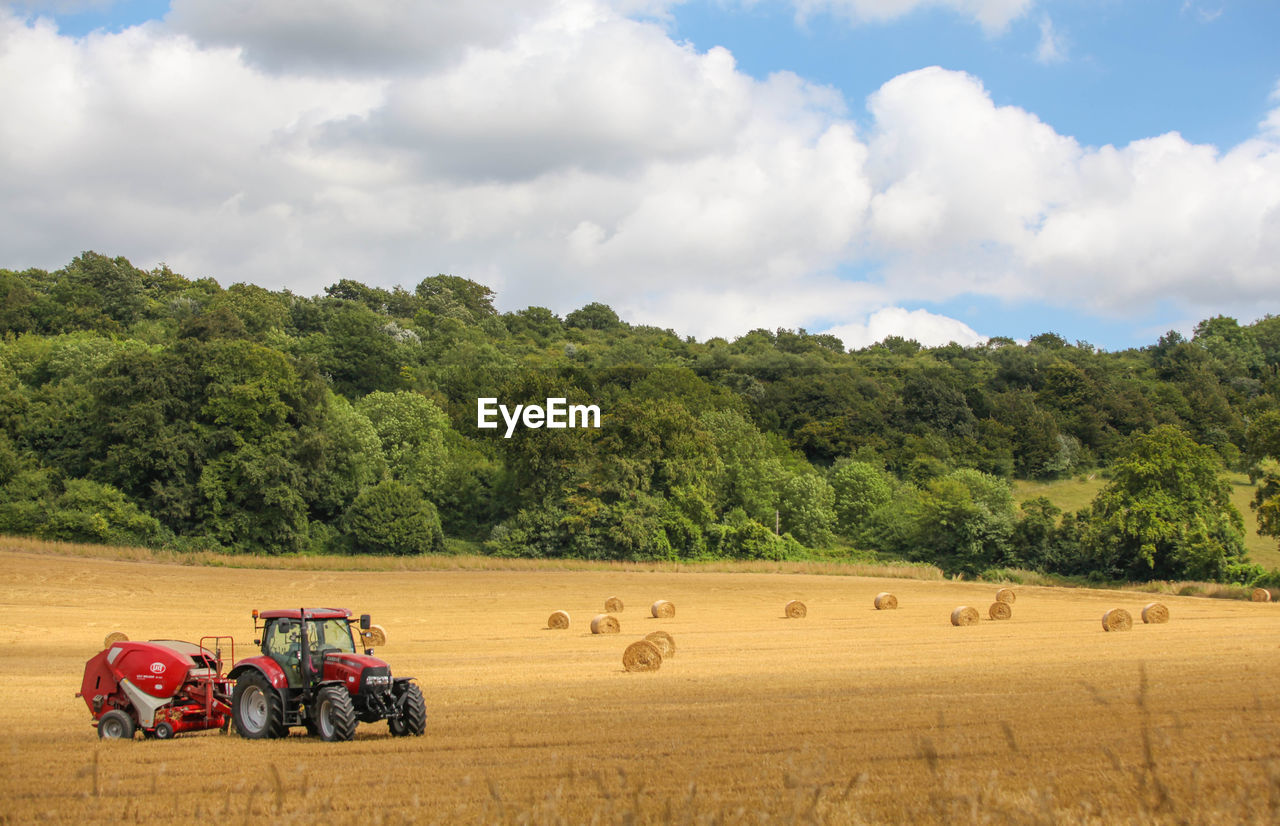 Red tractor by hay bales on field against trees