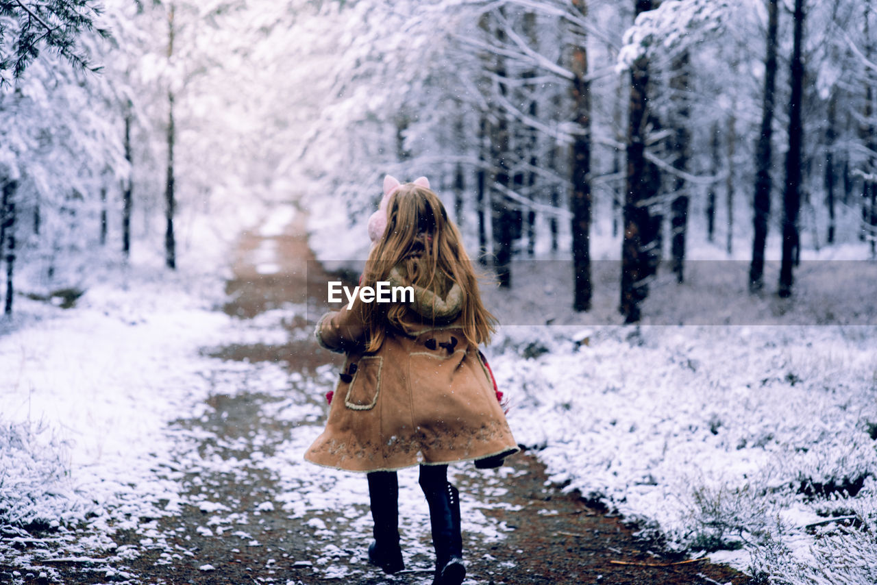 REAR VIEW OF WOMAN WALKING IN SNOW COVERED FOREST