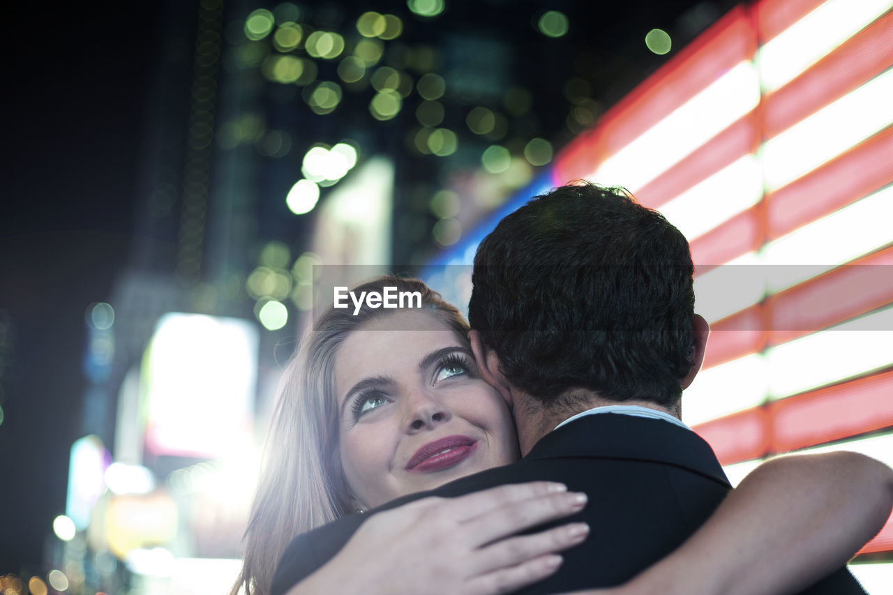 Beautiful woman embracing boyfriend by illuminated lights in city