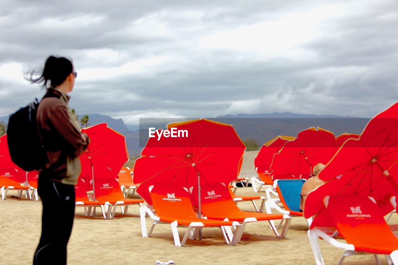 WOMAN WITH RED UMBRELLA AT BEACH AGAINST SKY