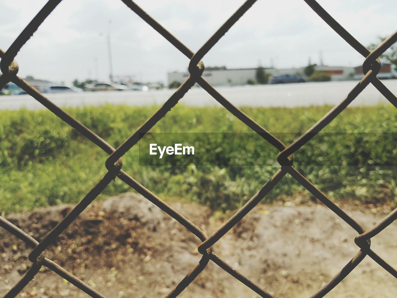 CLOSE-UP OF CHAINLINK FENCE IN FIELD AGAINST SKY