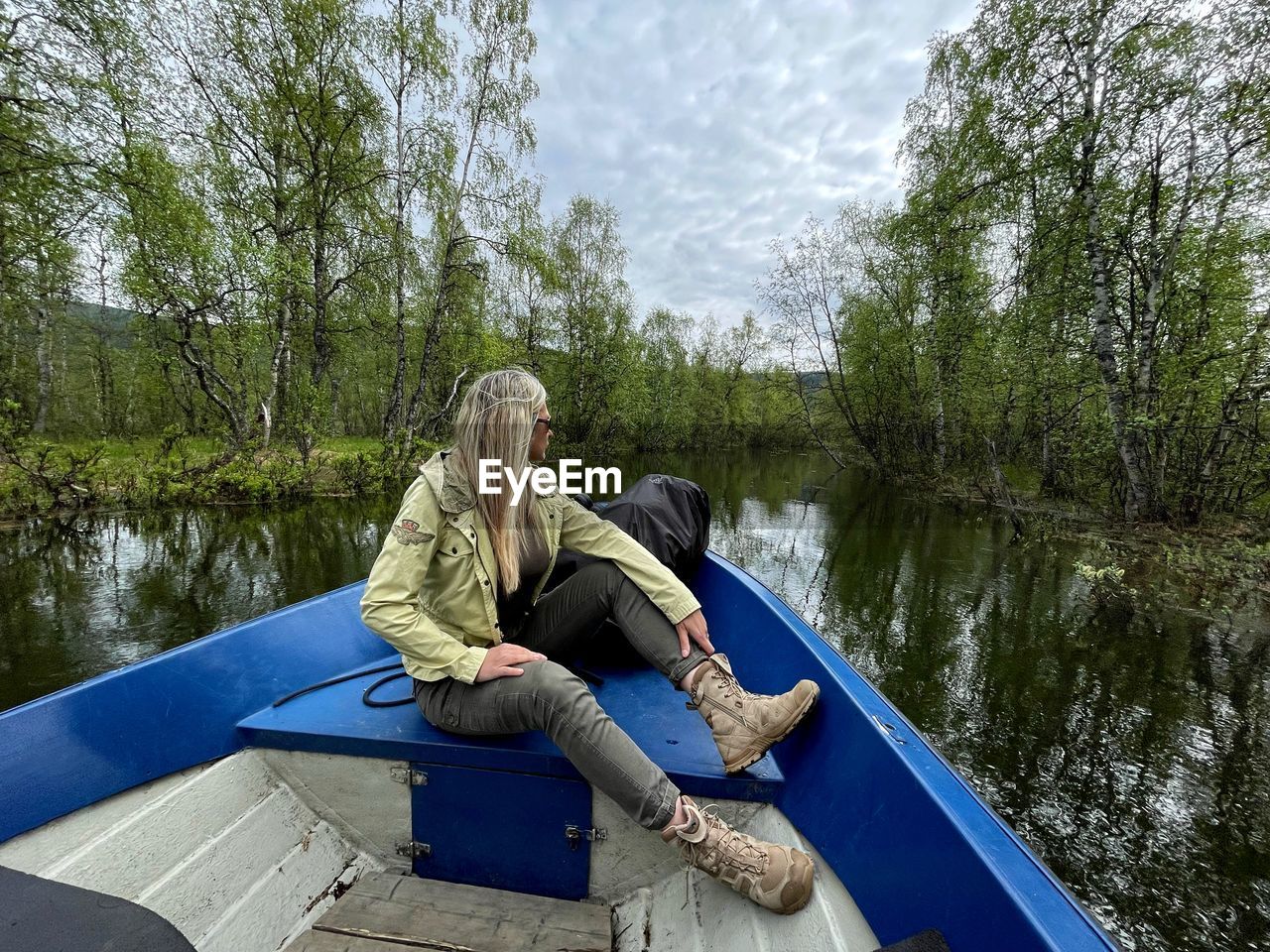 Woman sitting on boat in lake against trees