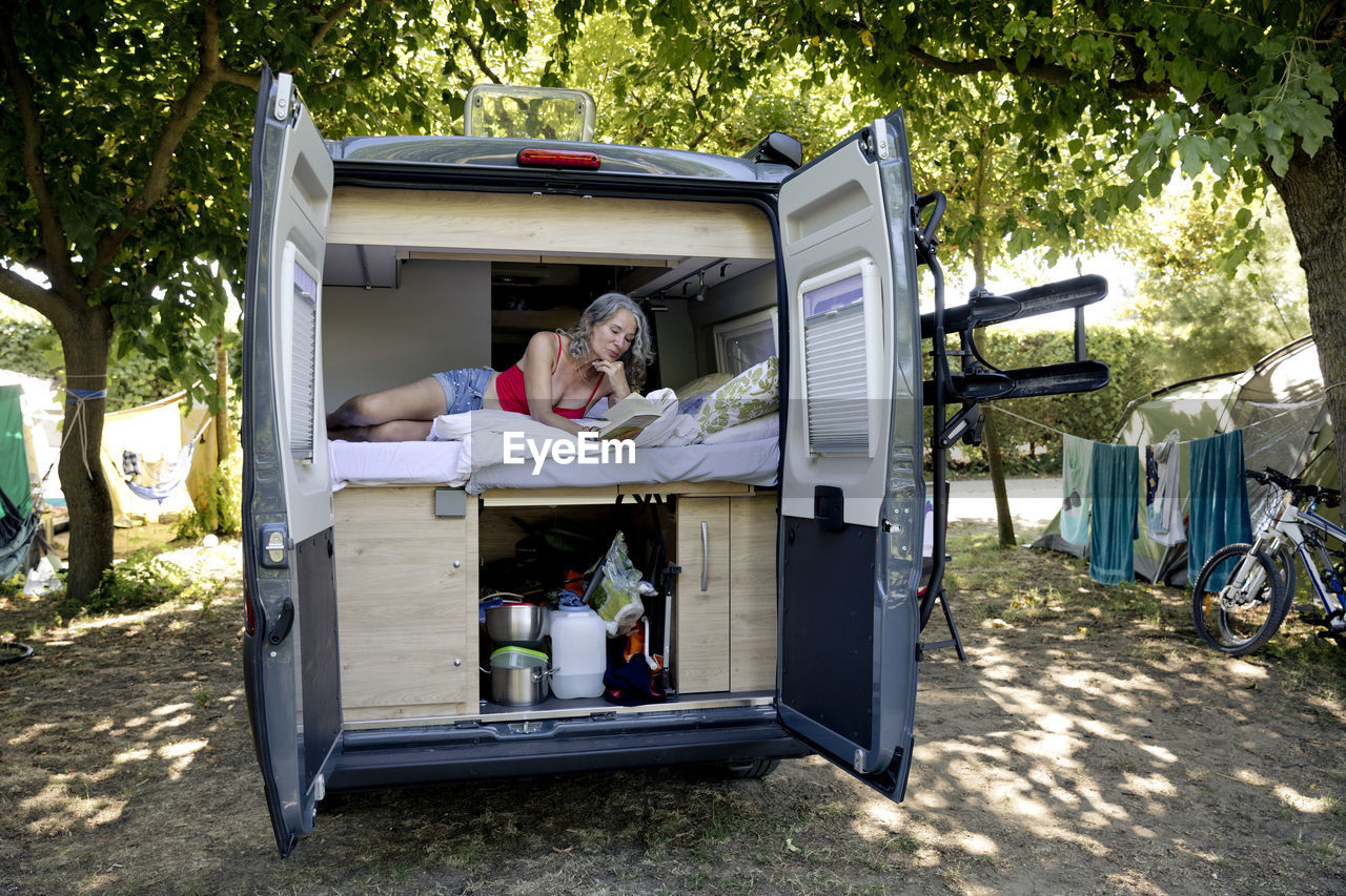 Senior woman lying in camper van reading book