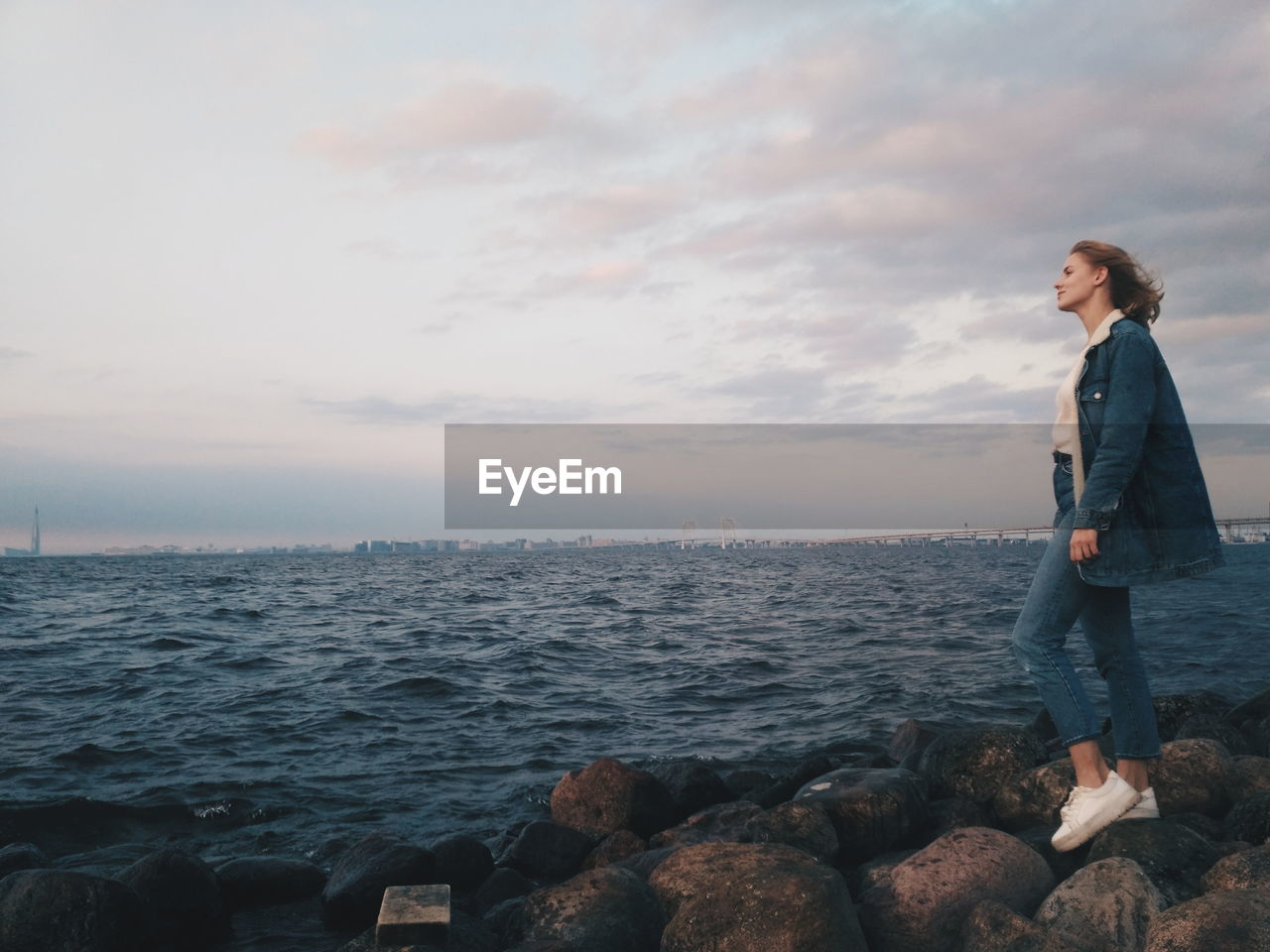 Woman standing on rock by sea against sky