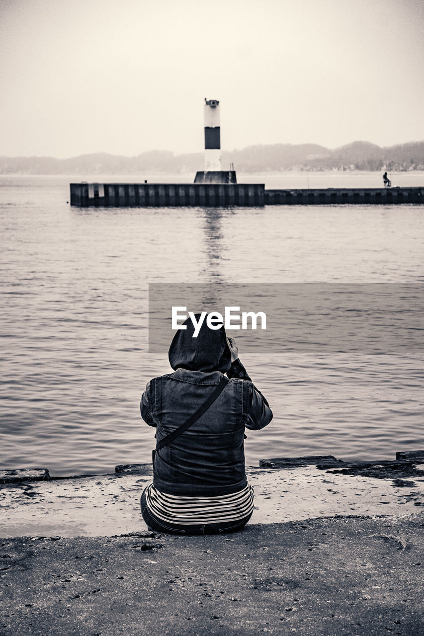 Rear view of person photographing lake while sitting on pier