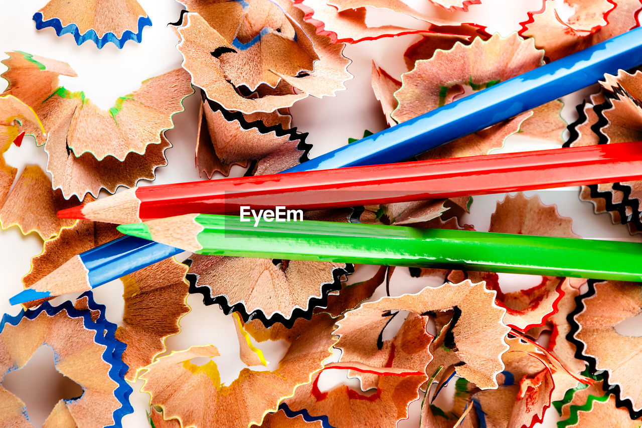 High angle view of multi colored pencils and shavings against white background