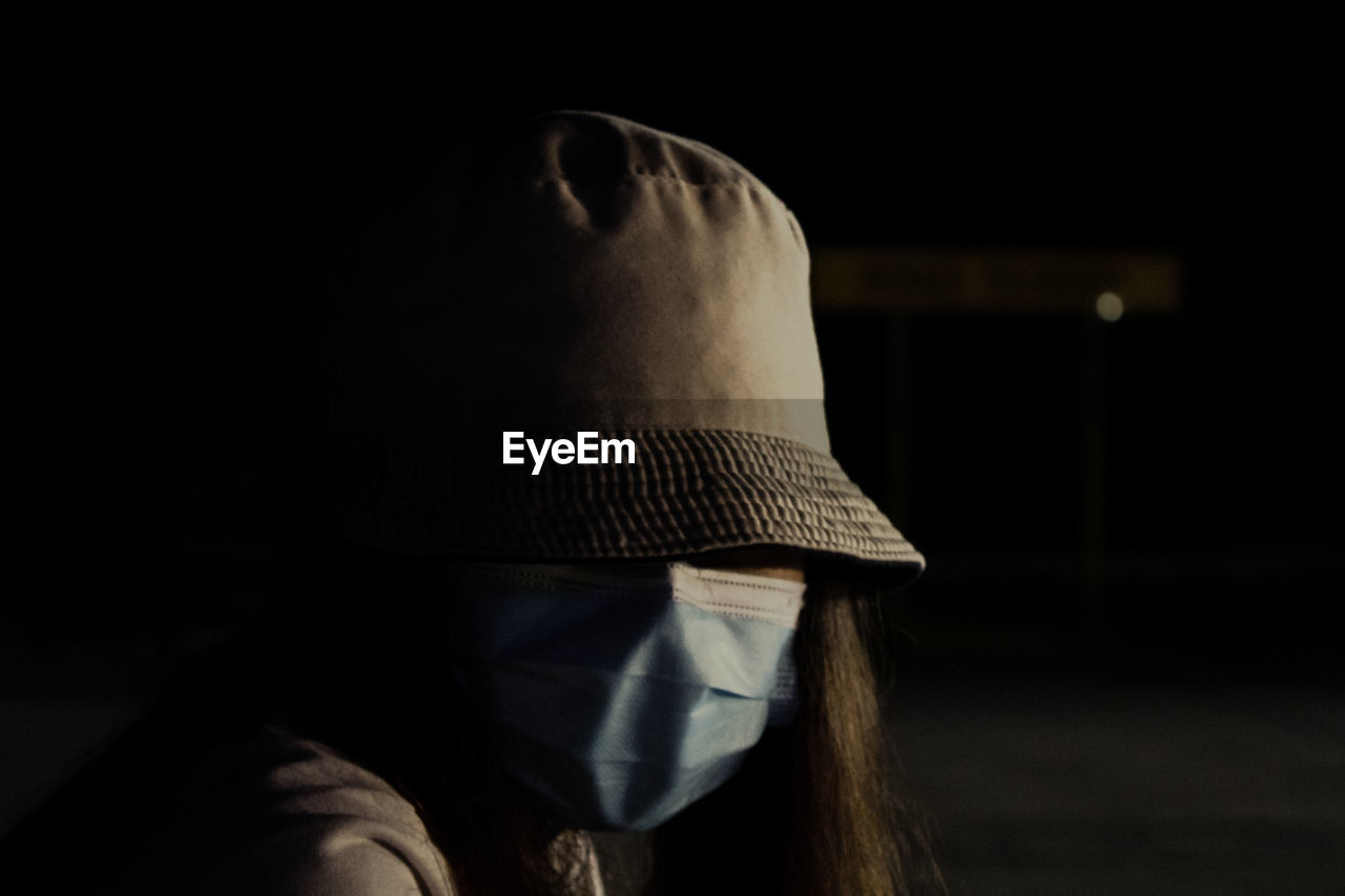 Close-up of young woman wearing mask sitting in darkroom