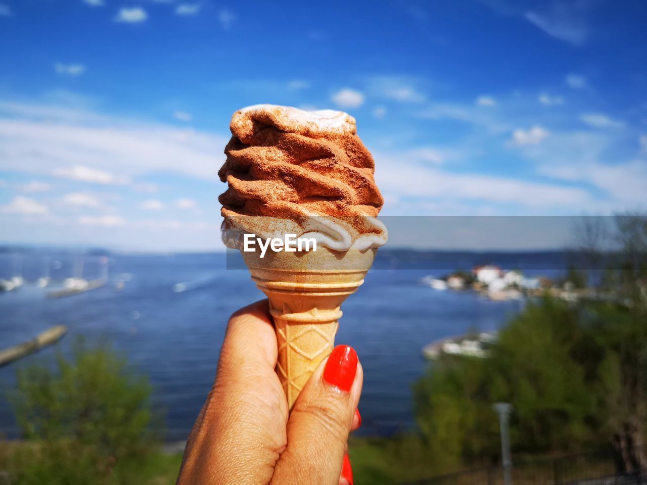 Close-up of hand holding ice cream cone against sky