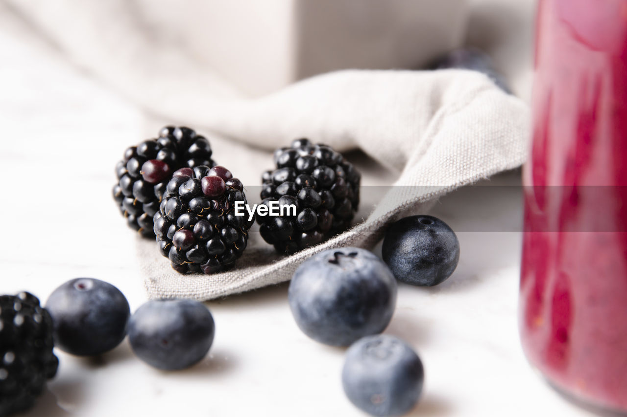 Close up detailed shot of blackberries beside blueberries and a gray linen cloth over a marble surface.