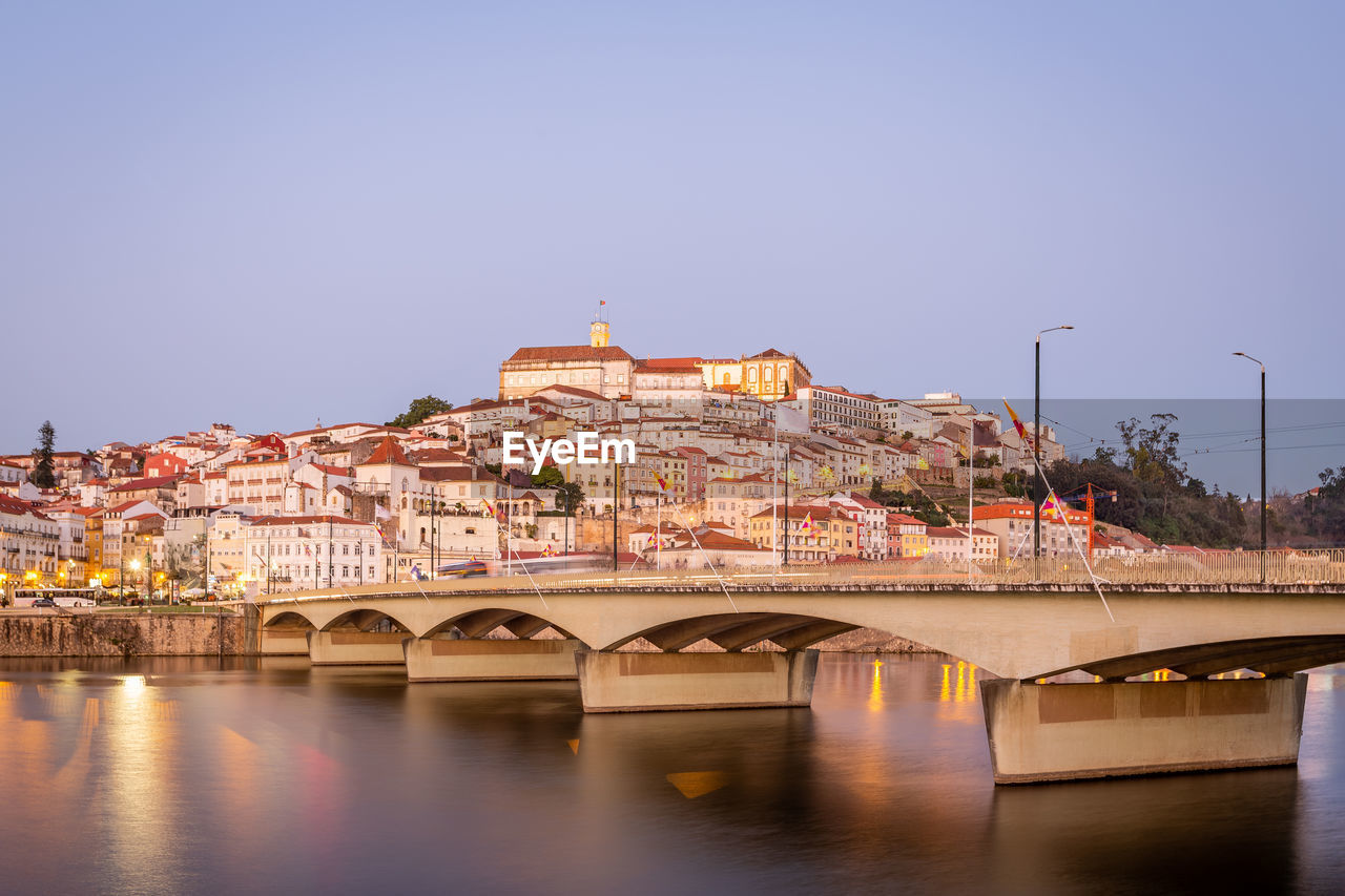 ARCH BRIDGE OVER RIVER AGAINST BUILDINGS IN CITY AGAINST CLEAR SKY