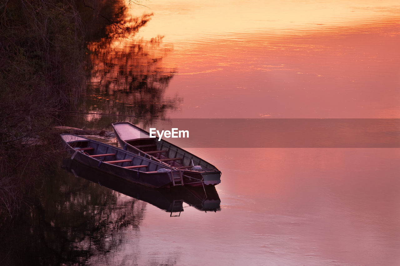 Boat moored in lake against sky during sunset