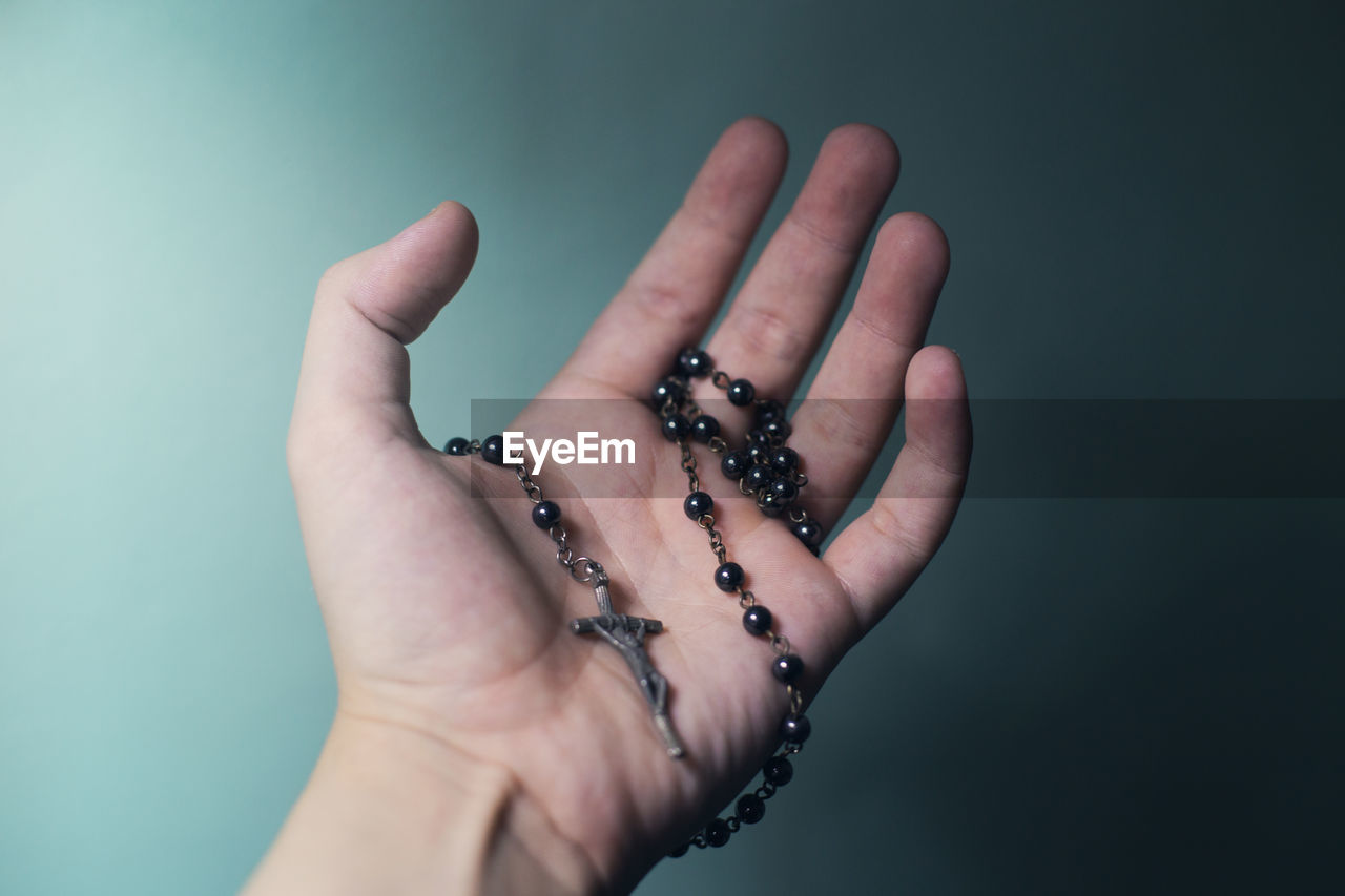 Cropped hand of person holding prayer beads against blue background