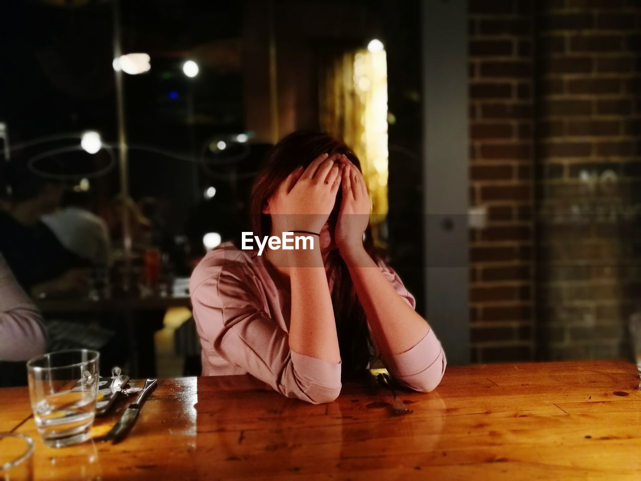 Woman covering face while sitting on chair at restaurant