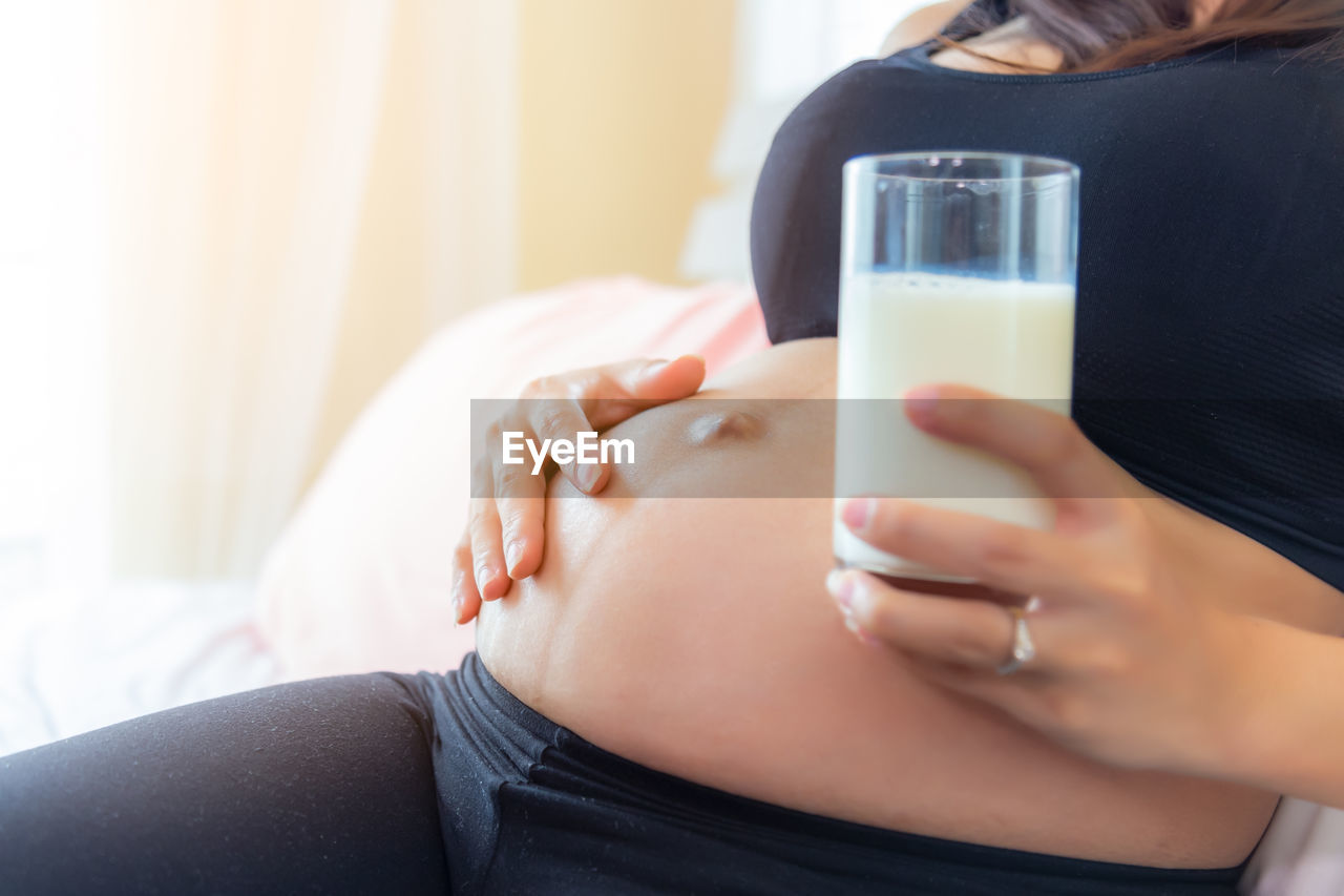 Midsection of pregnant woman holding milk in glass at home