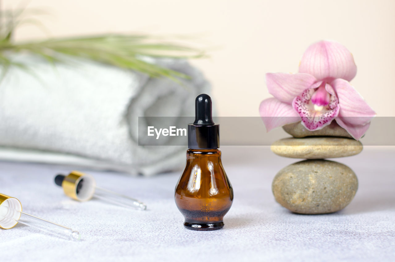 Composition of natural stones, orchid flower, rolled white towel and bottle of essential oil.