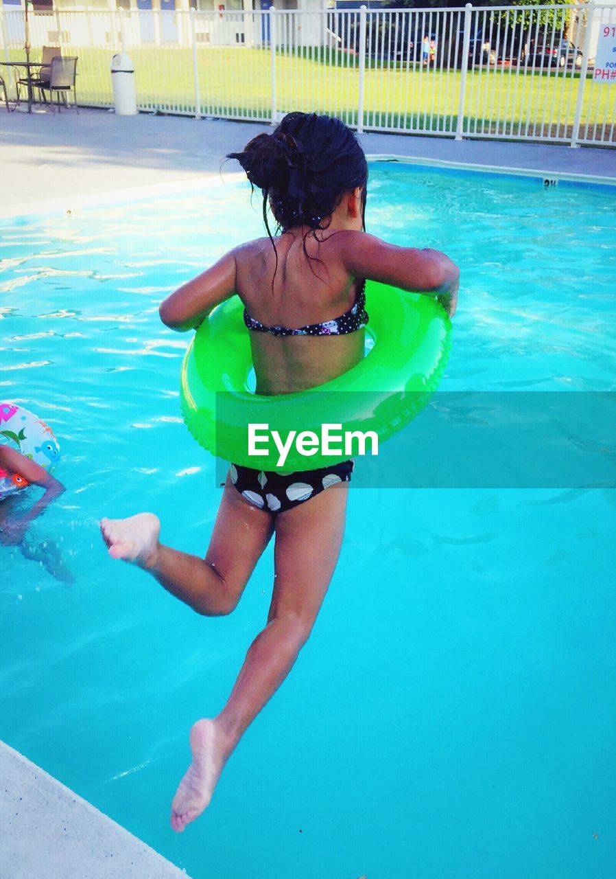 Rear view of girl with inflatable ring jumping in swimming pool