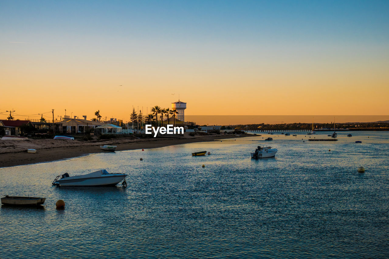 SAILBOATS MOORED IN HARBOR AGAINST SKY DURING SUNSET