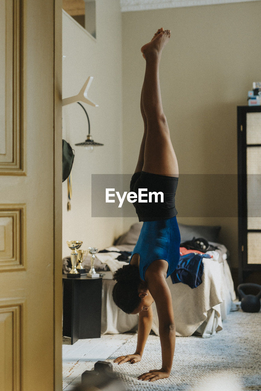 Female athlete doing hand stand in bedroom at home