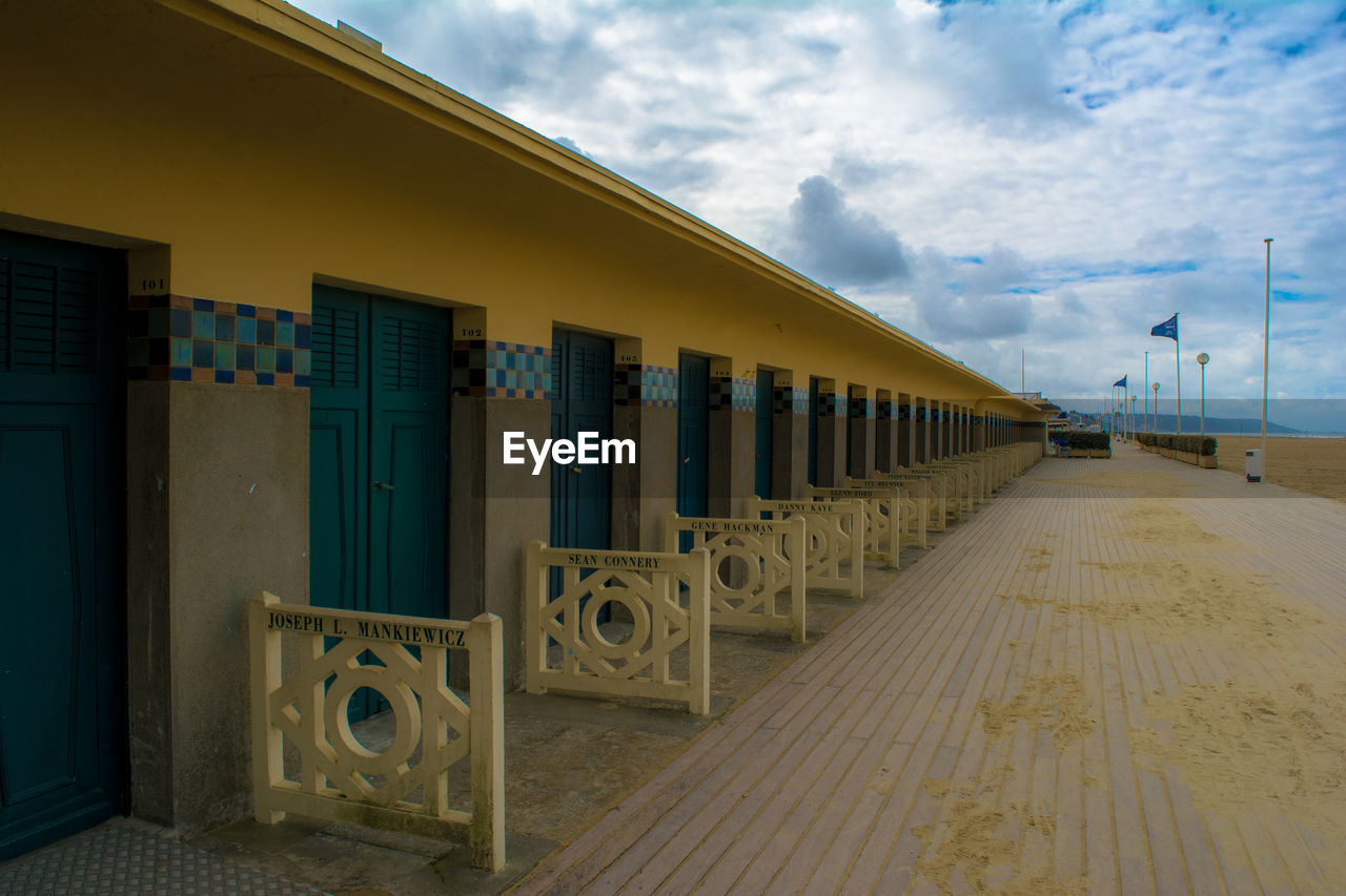 Walkway by building against cloudy sky