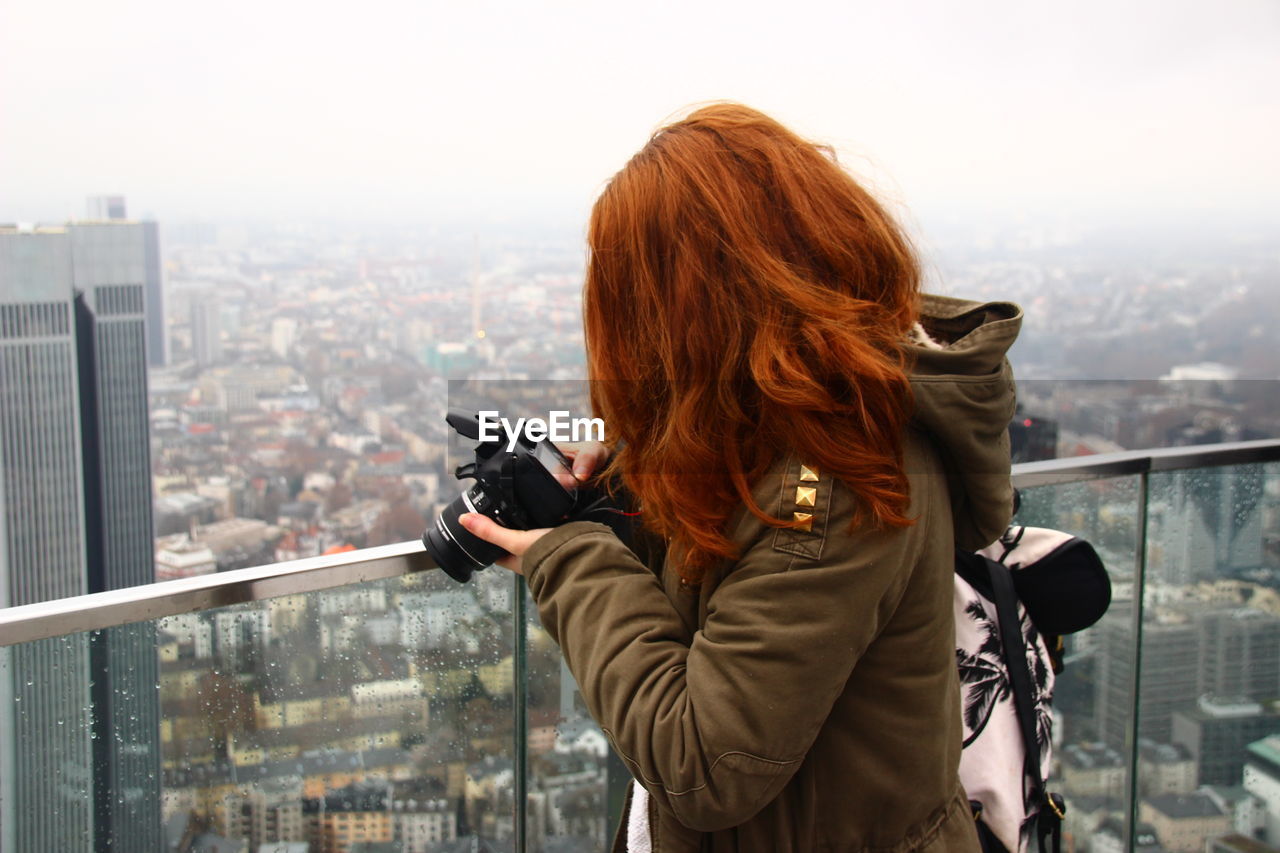 Side view of woman photographing with digital camera at balcony