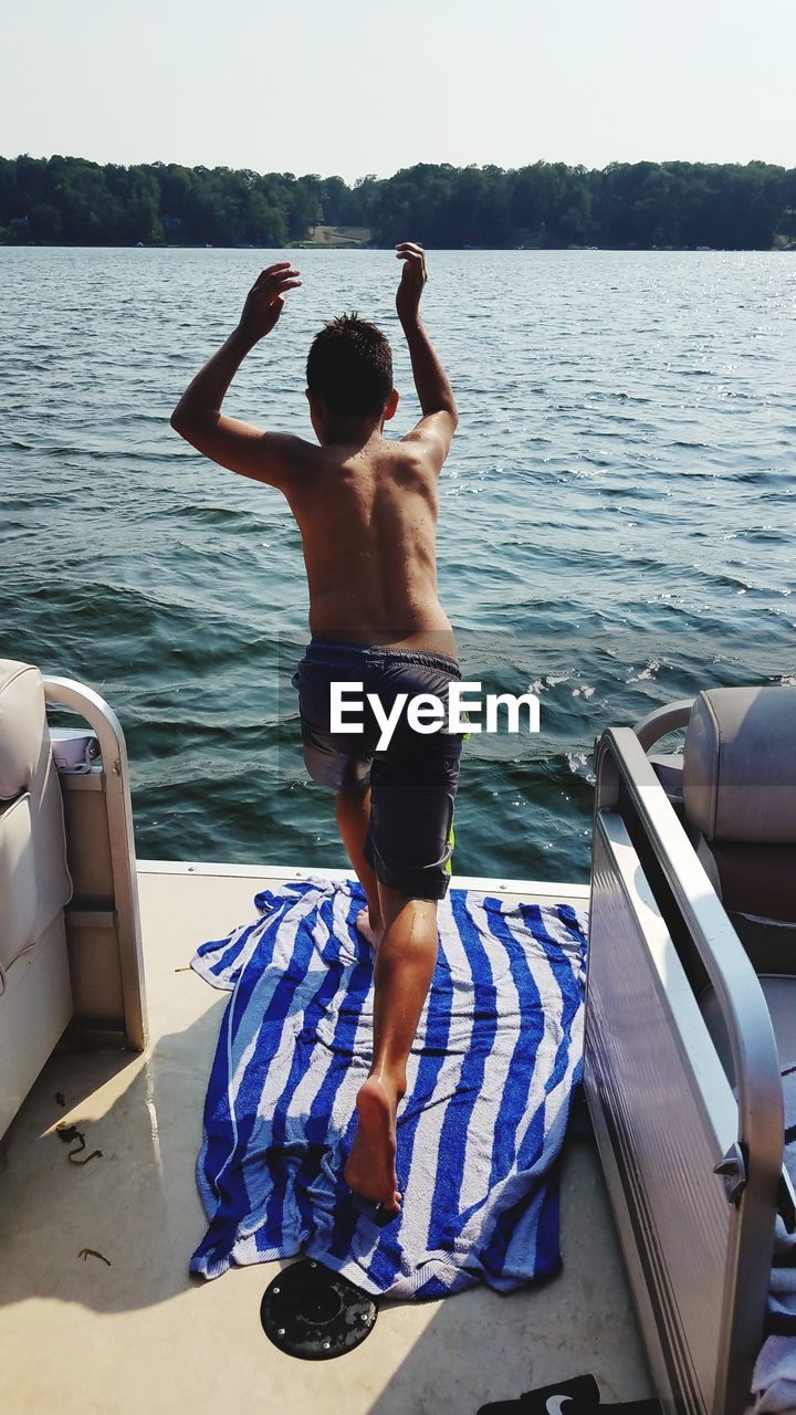Rear view of shirtless teenage boy diving in lake from boat against sky