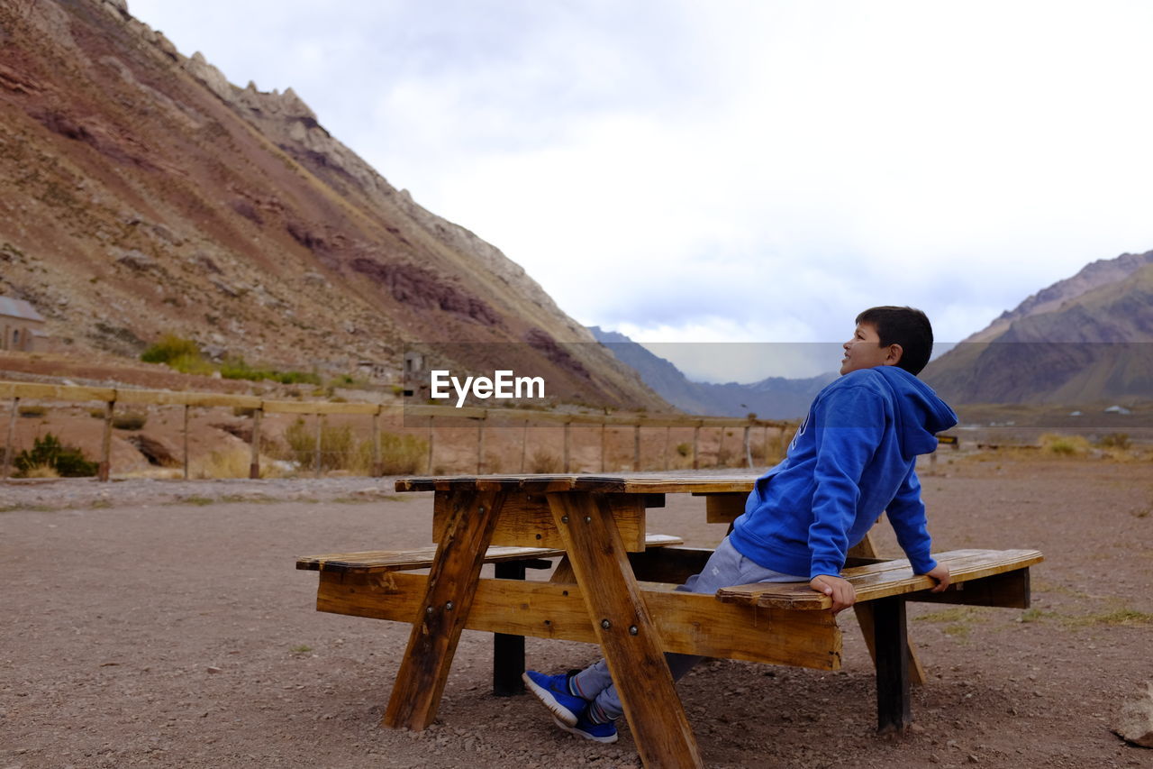 Boy looking away while sitting on seat against mountains