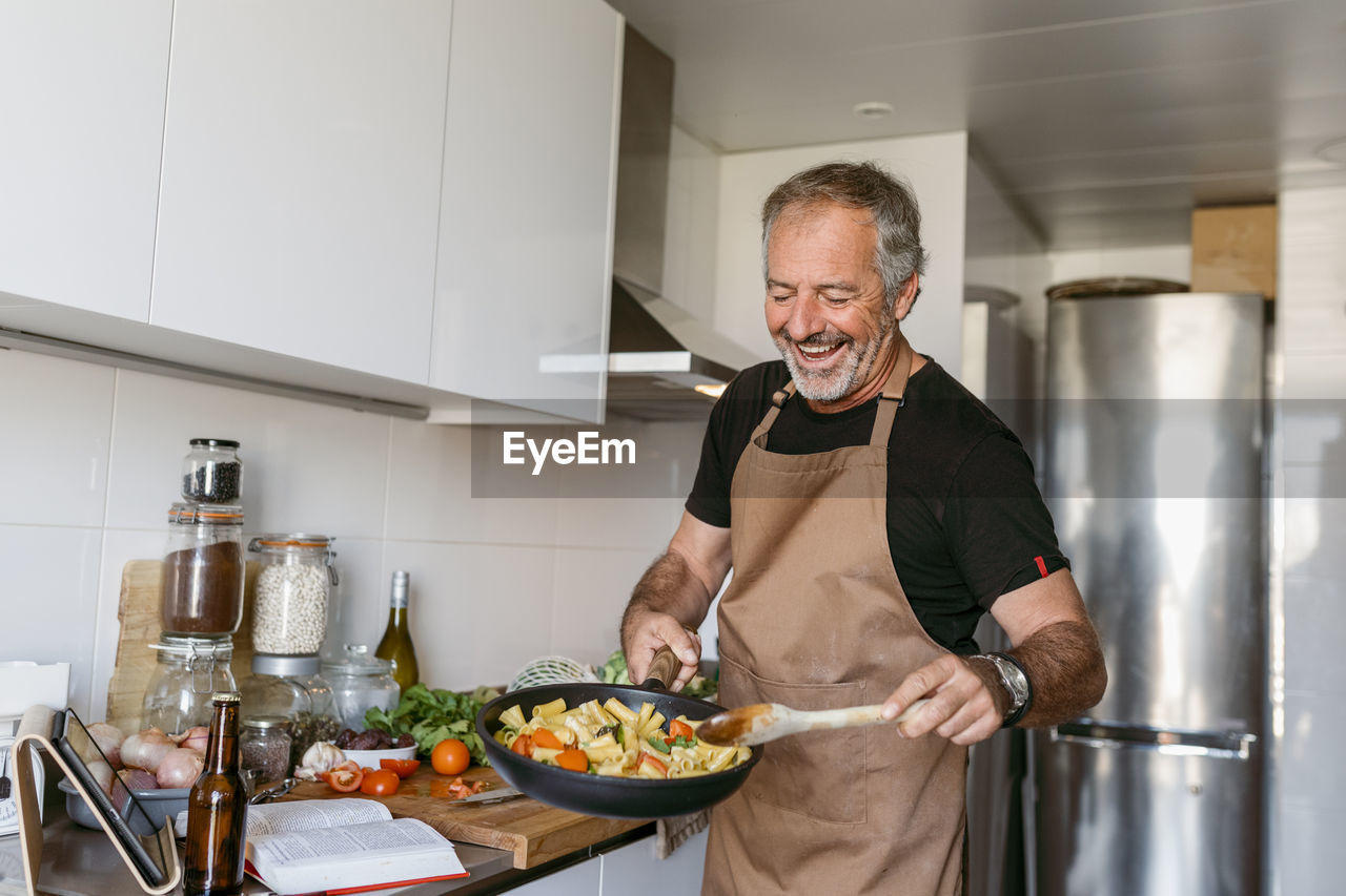 Smiling mature man preparing pasta while standing in kitchen at home