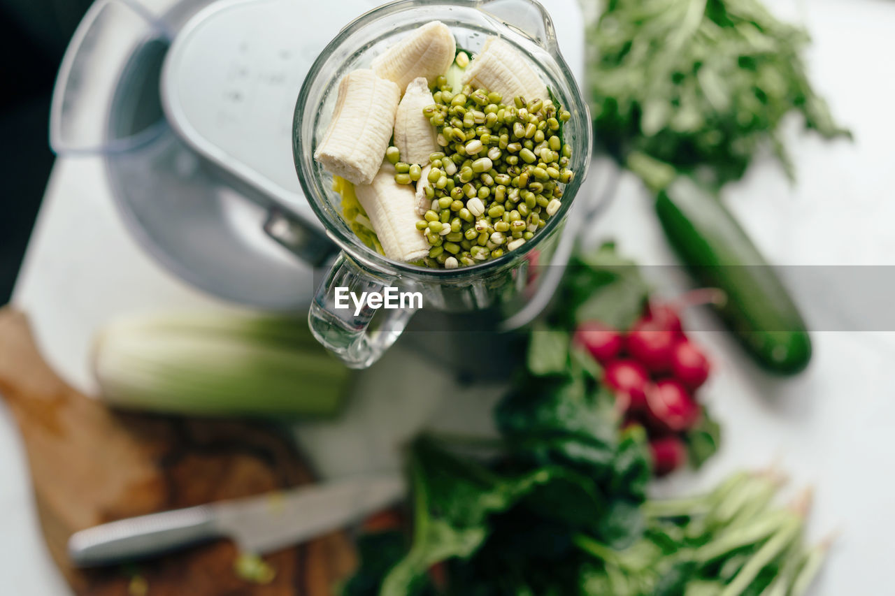 On the table is a blender filled with greens, vegetables and sprouted grains of mash. 