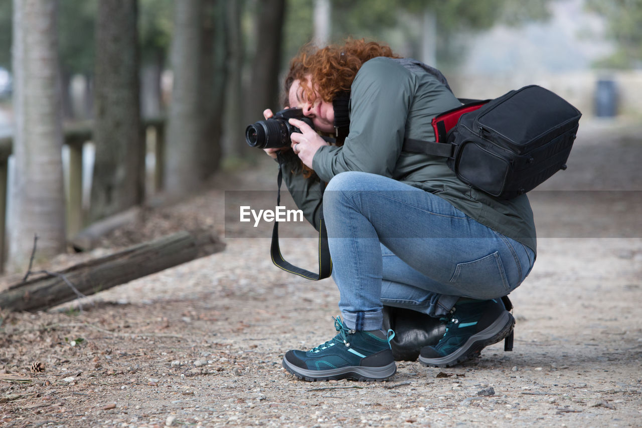 Full length side view of woman photographing with camera while crouching on land