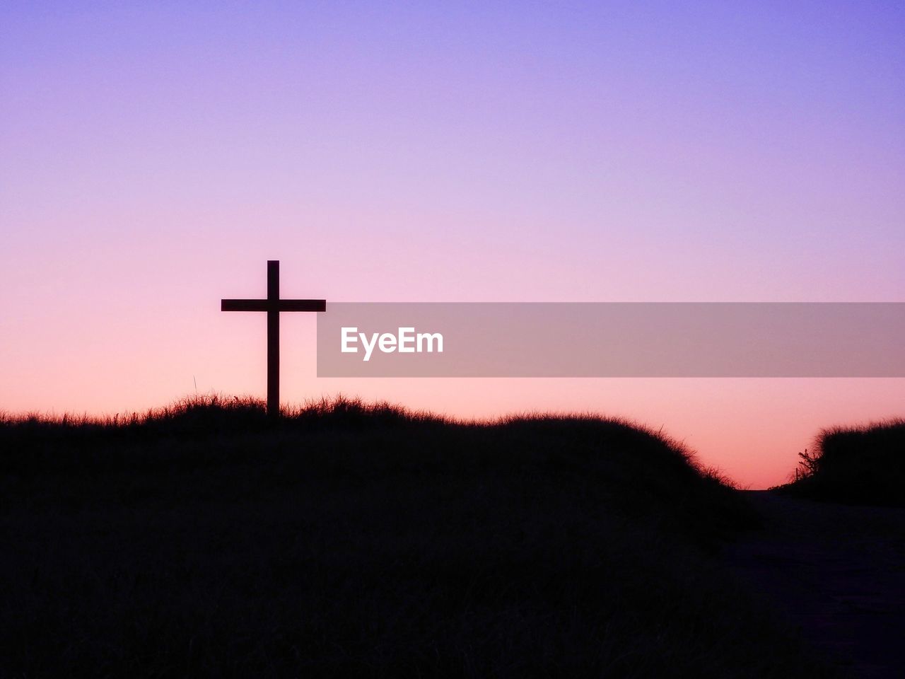 Low angle view of silhouette cross on hill against clear sky at sunset