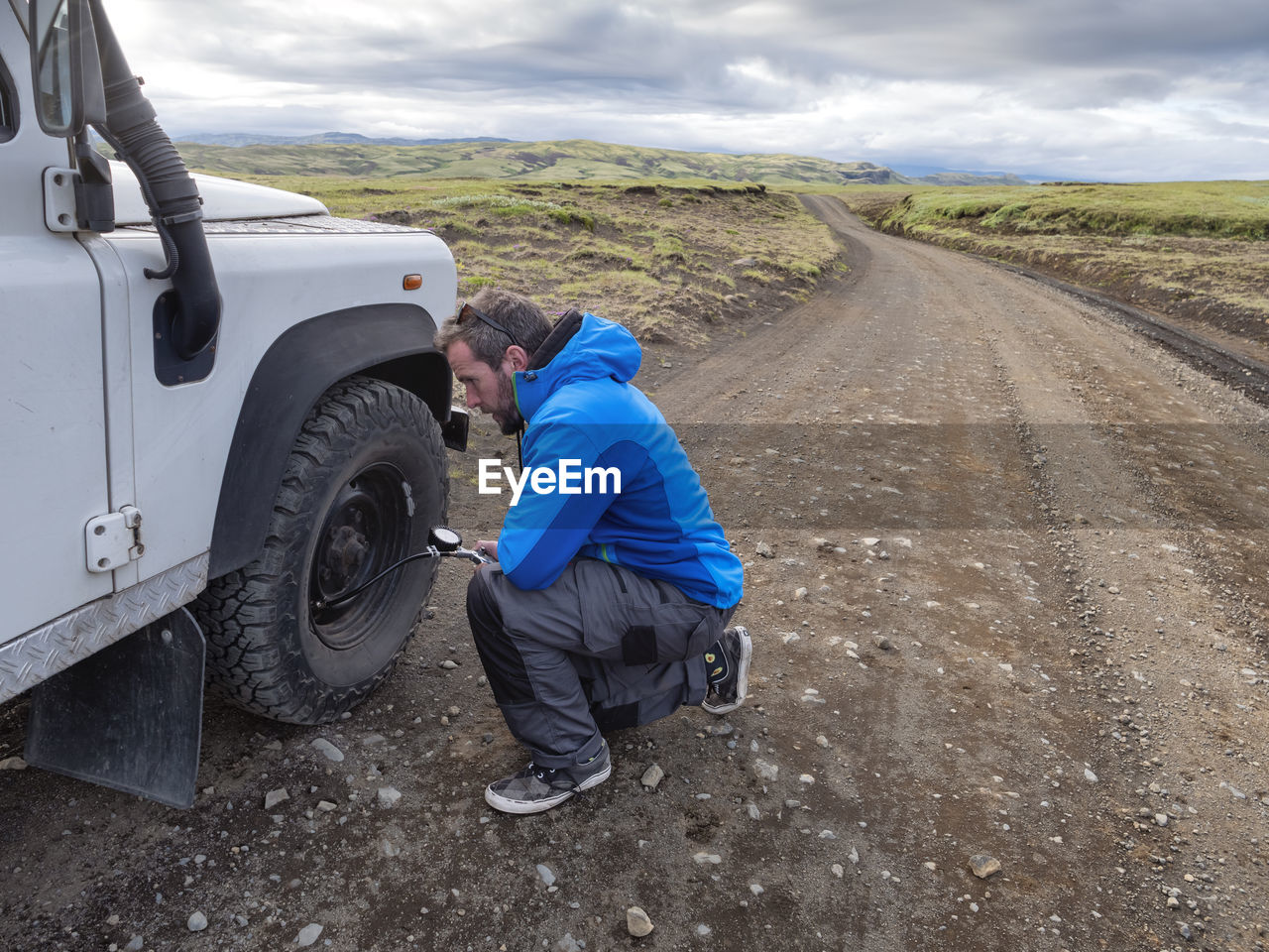 Man kneeling while examining tire pressure through equipment at roadside