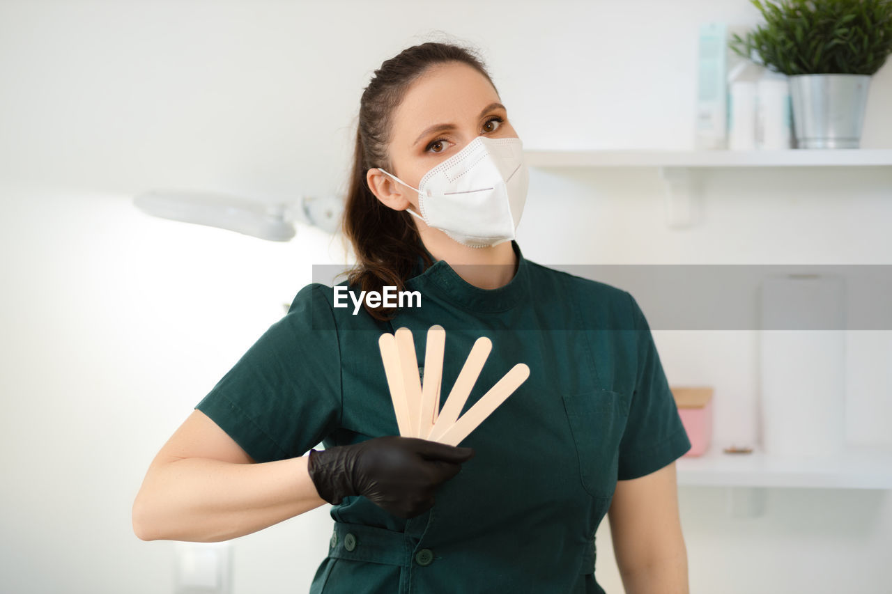 portrait of young woman wearing protective mask standing against wall