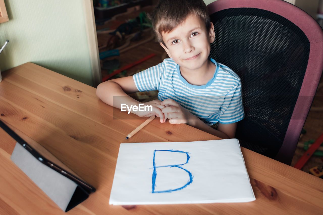 Happy child shows page with written letter b, home schooling