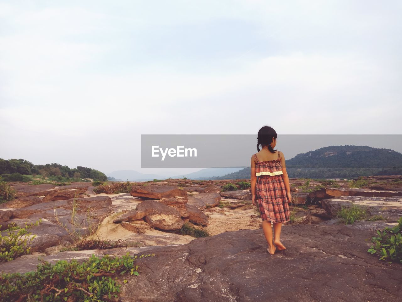 Rear view of girl standing on rock against sky