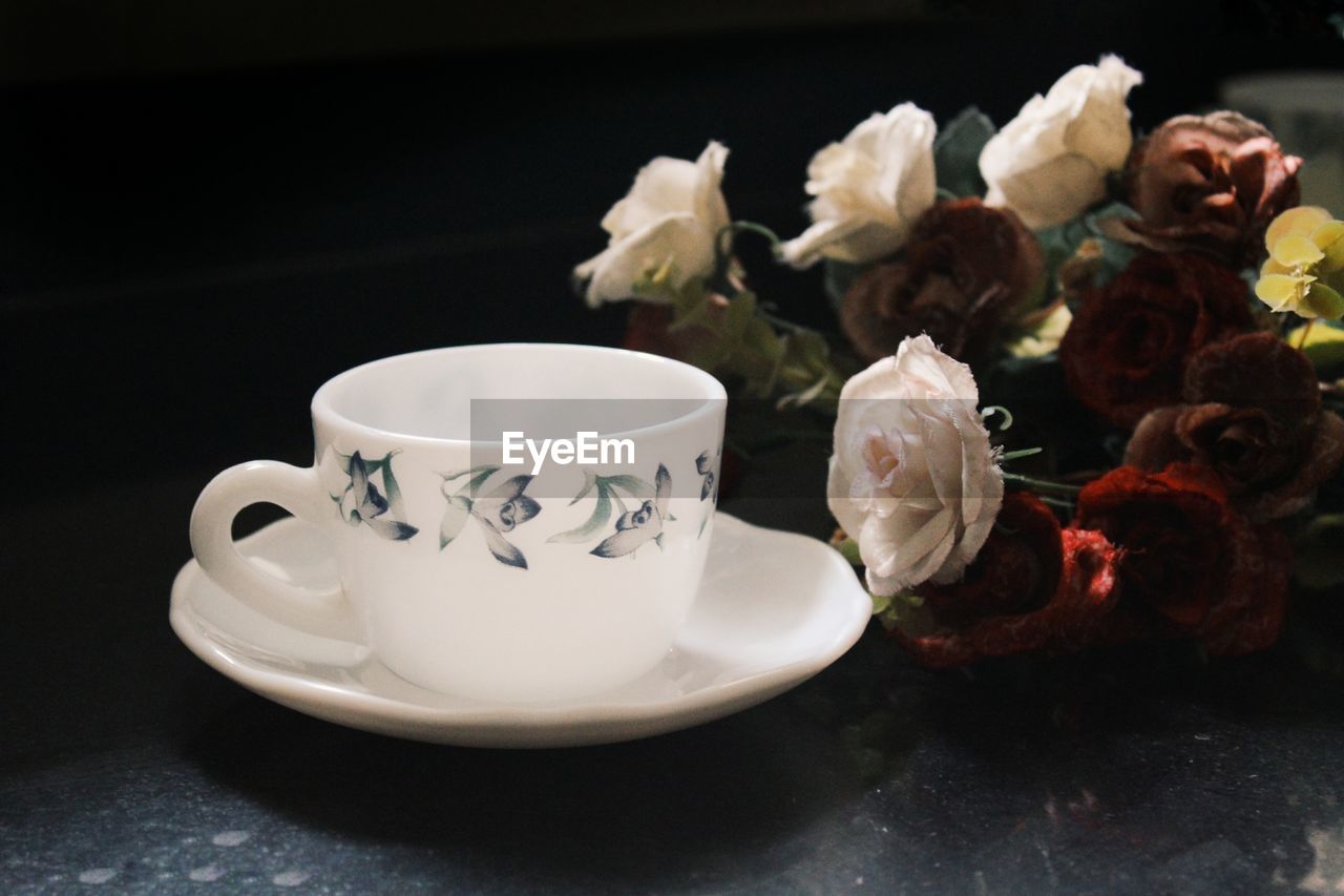 Empty cup by wilted roses on table
