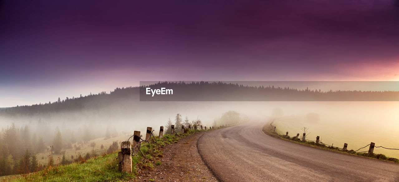 Road amidst trees against sky during foggy weather