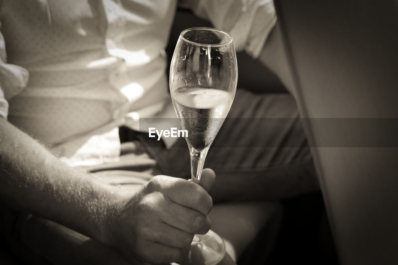 MIDSECTION OF MAN HOLDING WINE IN WINEGLASS