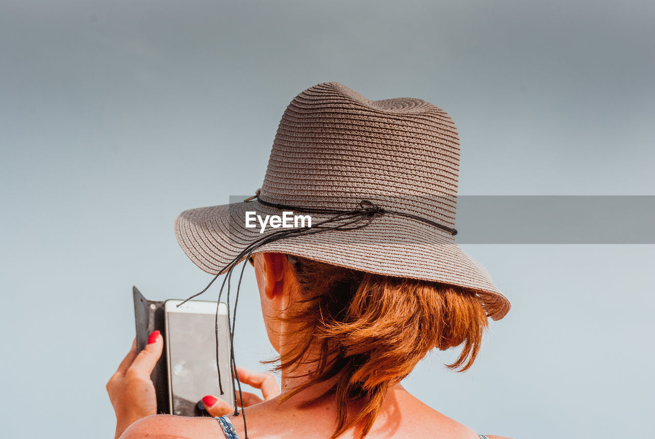 Rear view of woman using smart phone against clear sky